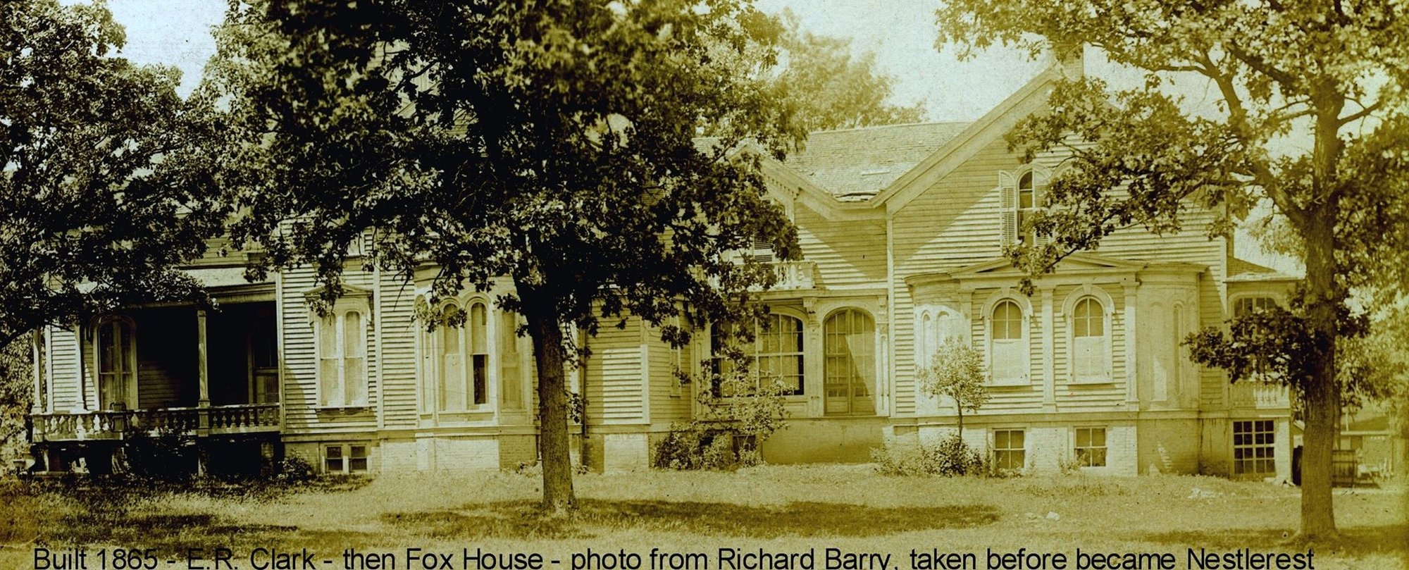 Long view of the house with porch, paired arched windows and raised foundation, captioned Built 1865 E.R. Clark then Fox House